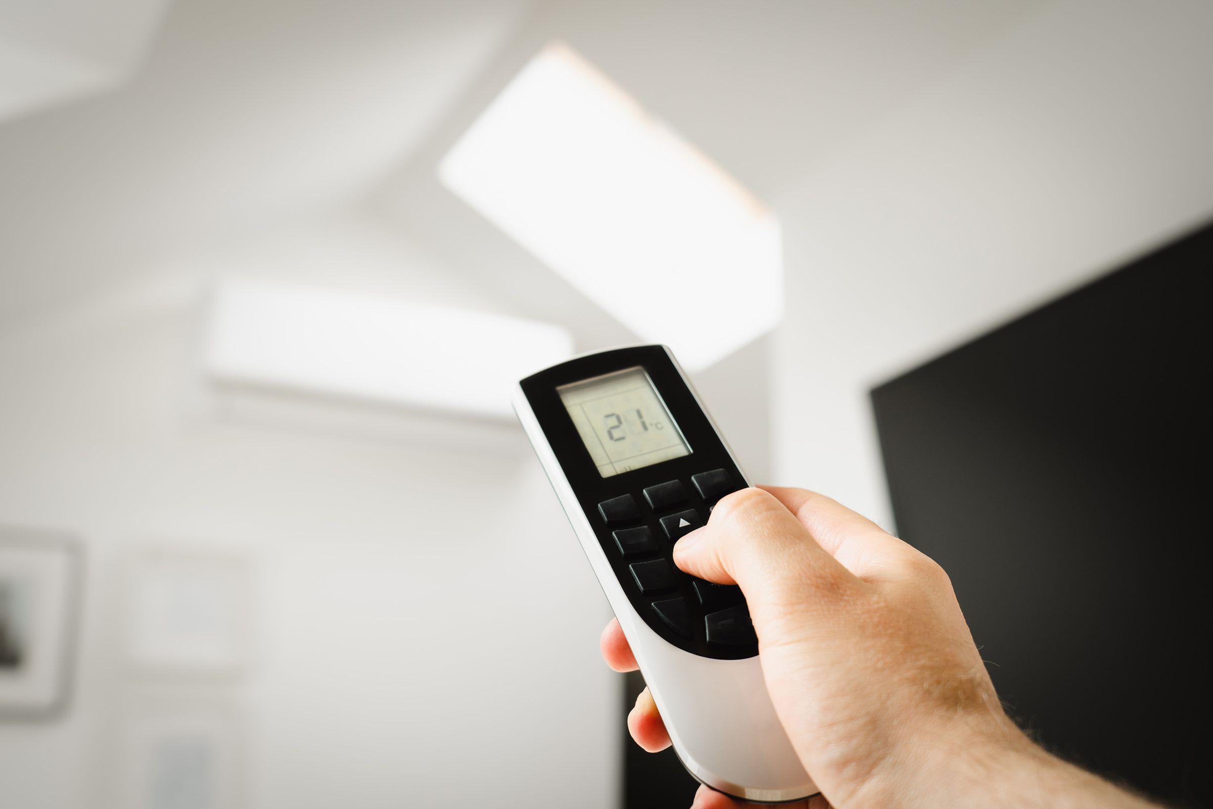 Main tenant une télécommande de climatiseur réglée à 21 degrés
